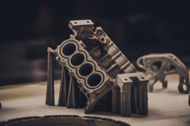 Metal 3D yazıcıya yazdırılmış nesneyi tutan adam.