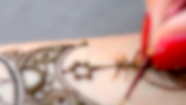 Fundo desfocado. Mestre colocar uma tatuagem de henna temporária na forma de folha closeup — Vídeo de Stock