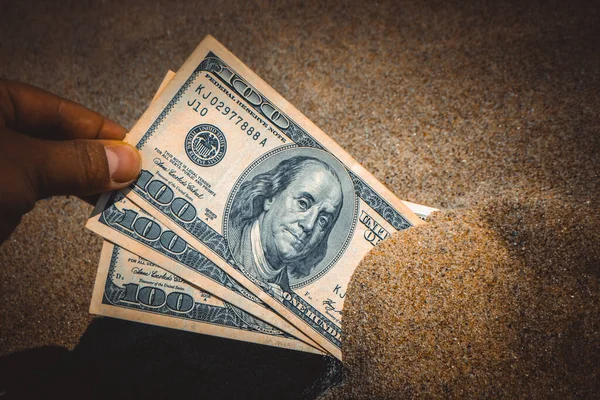 A girl takes out from the sand money notes of three hundred dollars.