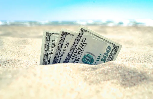 Peníze dolary napůl pokryté pískem leží na písečné pláži v blízkosti moře Stock Obrázky