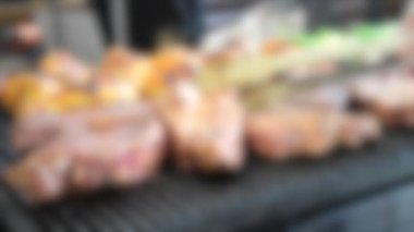 Arka plan bulanık. Adam biftekleri ve tavuk bacağını ızgaraya çeviriyor.