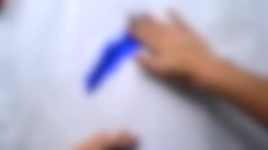Arka plan bulanık. Kız elleri beyaz kağıda mavi boya sürer..
