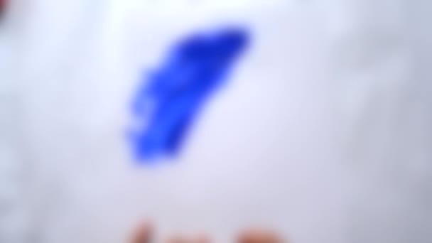 背景がぼやけている。女の子の手は白い紙の上に青色の塗料. — ストック動画