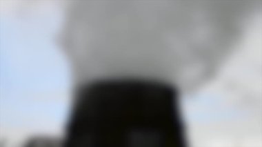 Arka plan bulanık. Büyük bir tüpün tepesinden bir sürü duman ve buhar yükseliyor.