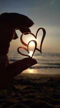 Gün batımında gün batımında güneşin arka planına karşı iki kalp şeklinde siyah çizgili parmakları olan kadın. Aşk delisi romantik sevgililer günü ruh hali ilişki dikey