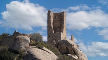 Eski taş kule ve kaleler mavi gökyüzünün altındaki kayalık tepenin üstünde.