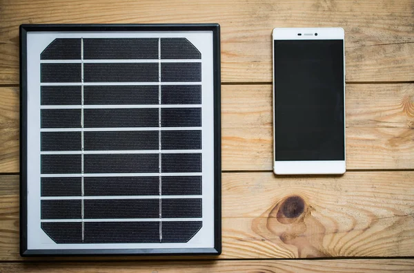 Panel słoneczny i smartphone na drewnianym stole — Zdjęcie stockowe