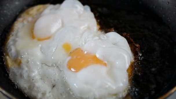 Two chicken eggs fried in a black frying pan on a gas stove. Slow motion. — Stock Video