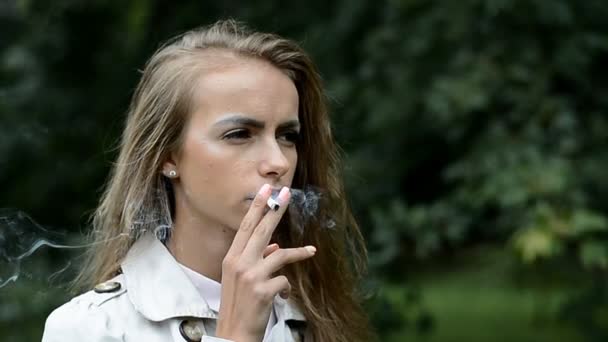 Портрет молодой женщины, курящей сигарету в городском парке — стоковое видео