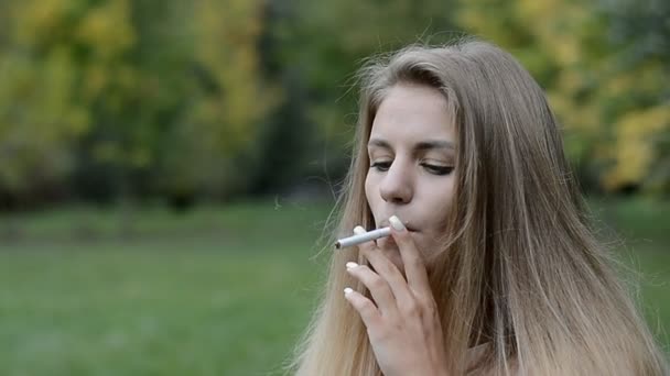 Porträt einer jungen Frau, die im Freien im sonnigen grünen Park Zigarette raucht. — Stockvideo