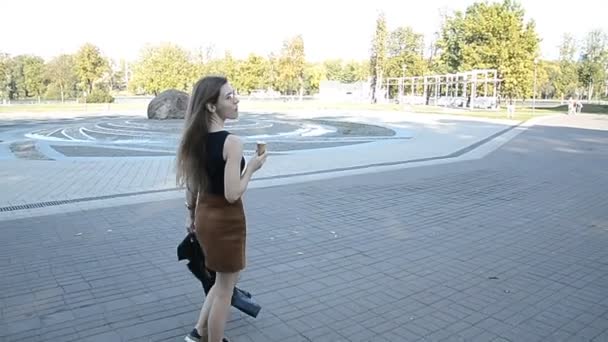 Mujer de pelo rizado caminando en el parque de la ciudad y comiendo helado — Vídeo de stock
