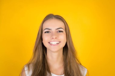 Neşeli ve sevimli bir gülümseme ile kameraya bakarak mutlu neşeli genç kadın. Stüdyo izole sarı boş stüdyo duvara vurdu.