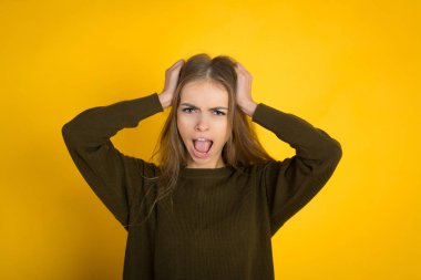 çapraz kolları poz ve kameraya sarı arka plan üzerinde seyir kazaklı güzel kadın