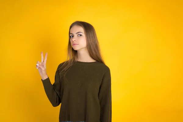 Retrato de jovem alegre mostrando dois dedos ou gesto de vitória, sobre fundo amarelo — Fotografia de Stock