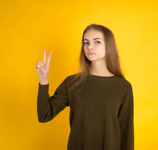 Mutatja a két ujjal vagy győzelme, gesztust, sárga háttér felett vidám fiatal nő portréja — Stock Fotó
