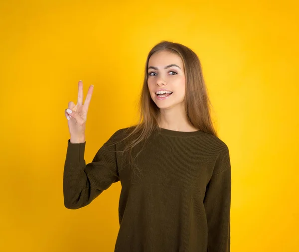 Портрет веселої молодої жінки, що показує два пальці або жест перемоги, на жовтому тлі — стокове фото
