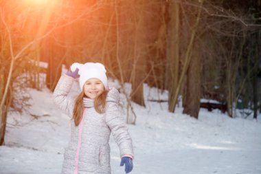 Komik küçük kız kar yağarken güzel kış parkında eğleniyor.