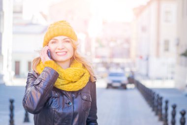 Güzel iş kadın bir örme şapka ve sarı örme eşarp yürüyor ve telefonda görüşmeler