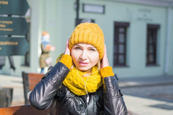 Portrait of a very attractive woman in a knitted hat and scarf with headphones in the ears on a city street — Fotografia de Stock