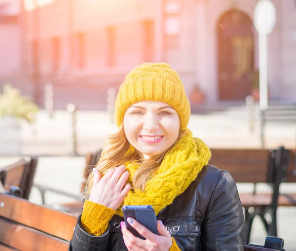 portrait of a young attractive woman in a knitted hat and knitted scarf, which sits on a bench in the city park