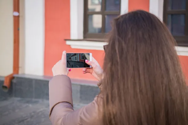 Young woman taking pictures of building. Old house in phone lens