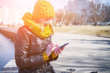 Sokakta odaklanmamış bir arka plan ile bir akıllı telefon kullanan mutlu kadın