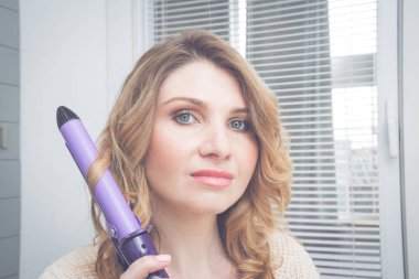 Güzel genç sarışın kadın yan görünümü AynaHDD ona yansıma bakarak onu Curling demir Tong kullanarak