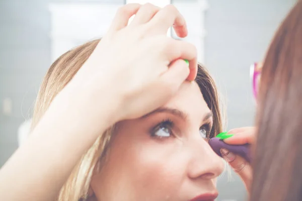 Ung blondine kvinde, der anvender makeup til model i salon - Stock-foto