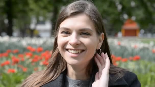 Attraktiv kvinna ansikte närbild skrattar i bakgrunden Röda tulpaner, stadsparken på våren, sommaren eller hösten — Stockvideo
