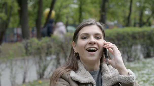 Happy and surprised beautiful brunette girl talking on the phone on city street — Stock Video