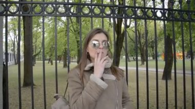 bir ceket ve güneş gözlüğü güzel kız parkta sigara içiyor