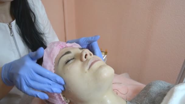 Cosmetologist que limpa a pele paciente na clínica de beleza que aplica uma máscara de creme — Vídeo de Stock