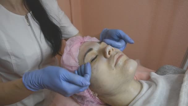 Cosmetóloga femenina concentrada está haciendo masaje facial — Vídeo de stock