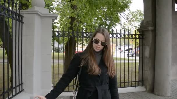 Fiatal lány fekete kabátban cigizik a városban. — Stock videók