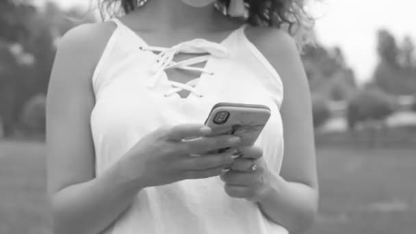 Mujer manos mensajes de texto en el teléfono en un parque de imágenes en blanco y negro — Vídeo de stock