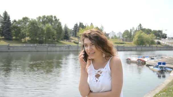Όμορφη νεαρή γυναίκα έχοντας μια τηλεφωνική συνομιλία σε ένα πάρκο — Αρχείο Βίντεο