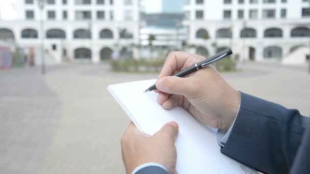 Hombre de negocios en vista urbana tomando notas en un cuaderno de papel plan de negocios — Vídeo de stock