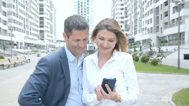 Hermosa joven mujer de negocios muestra opciones interesantes en su teléfono a un hombre de negocios y discutir caminos de desarrollo juntos . — Vídeo de stock