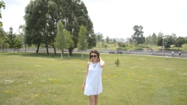 Menina bonita em um vestido de verão branco e cabelo encaracolado caminha em um parque de verão — Vídeo de Stock