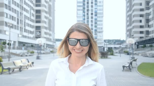 Retrato de una hermosa chica rubia en gafas de sol en la ciudad moderna en el fondo — Vídeo de stock