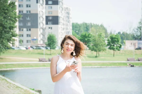 Mooi meisje met een mobiele telefoon loopt door een stadspark op een warme zomerdag — Stockfoto