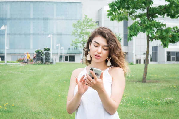 Un retrato de una hermosa mujer sonriente con el pelo rizado mensajes de texto con su teléfono — Foto de Stock