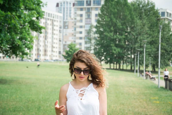 Menina bonita em um vestido branco no parque da cidade de verão olha para baixo — Fotografia de Stock