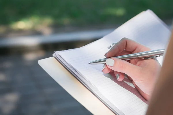 female hand takes notes in a notebook in nature