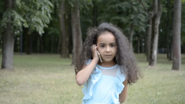 美しい5歳の小さなアフリカの女の子は 都市公園のHd映像で美しい夏の日に携帯電話で話しています — ストック動画