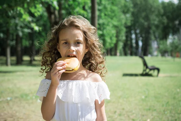 Carino bambina mangiare un hamburger o cheeseburger — Foto Stock