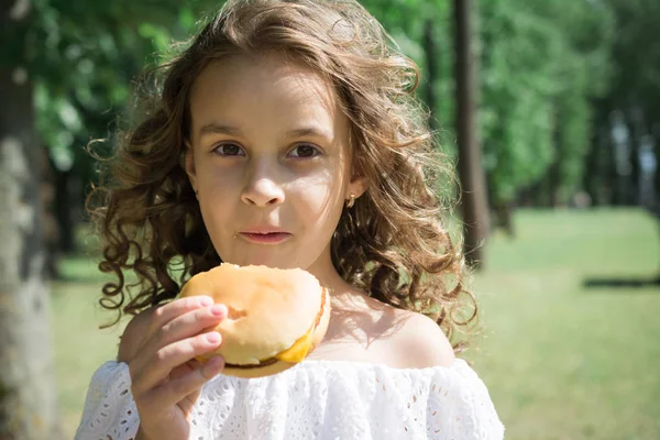 Carino bambina mangiare un hamburger o cheeseburger — Foto Stock