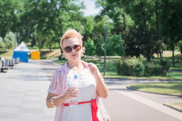 Hot weather concept, beautiful stylish girl with a bottle of water in the city streets — стоковое фото