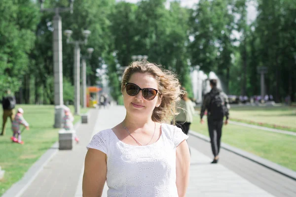 Retrato de una niña con un vestido blanco y gafas de sol en el parque de la ciudad — Foto de Stock