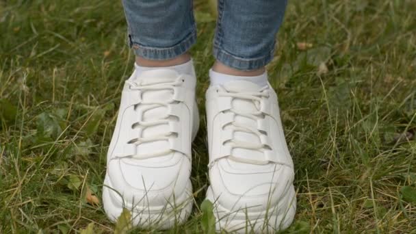 Хипстерские женские ноги в белых кроссовках на зеленой лужайке — стоковое видео